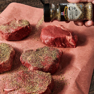 ['McCormick Grill Mates seasoning being sprinkled on raw steaks.']