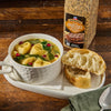 ['A bowl of soup with tortellini, spinach, and pomegranate seeds, a plate with two pieces of bread, a spoon, and a container of McCormick Grill Mates Cracked Black Pepper &amp; Garlic seasoning.']