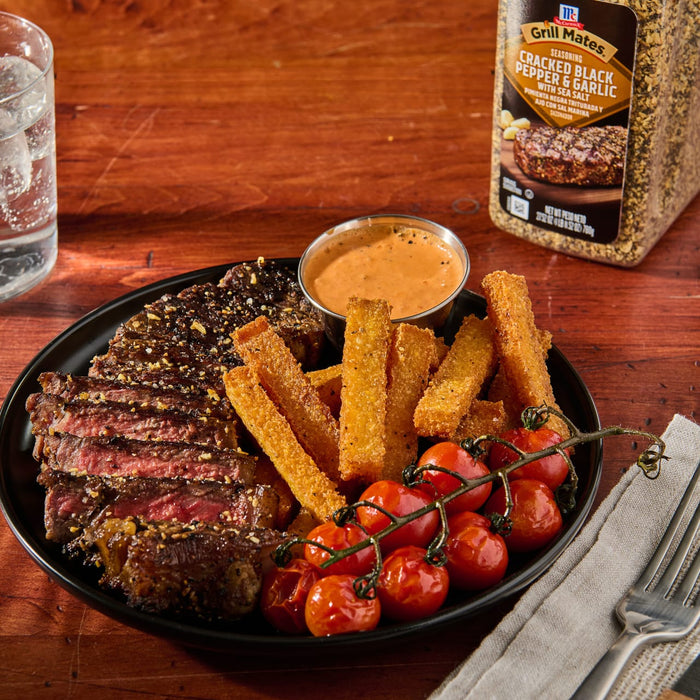 ['A plate of grilled steak, fried polenta sticks, and cherry tomatoes with a side of dipping sauce and a container of McCormick Grill Mates Cracked Black Pepper &amp; Garlic seasoning.']