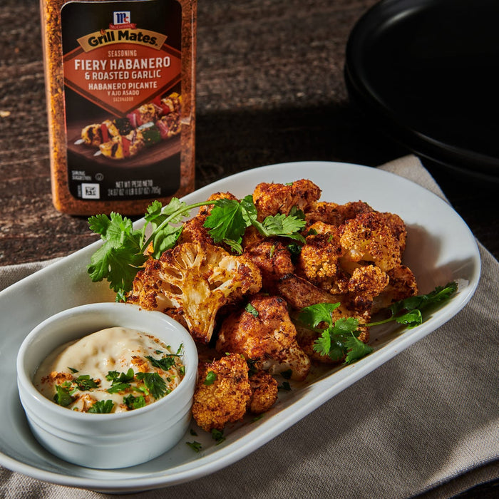 ['A plate of roasted cauliflower florets seasoned with McCormick Grill Mates Fiery Habanero &amp; Roasted Garlic seasoning and served with a side of dipping sauce.']