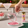 A hand sprinkles Great Value brand red sprinkles onto a white frosted dessert in a baking pan.