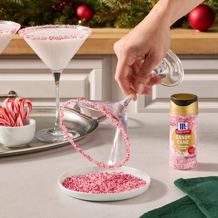 A hand sprinkles Great Value brand red sprinkles onto a white frosted dessert in a baking pan.