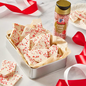 McCormick Candy Cane Toppers adorn pieces of white chocolate bark in a metal tin, surrounded by red and white ribbons.
