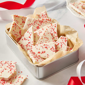 McCormick Candy Cane Toppers adorn pieces of white chocolate bark in a metal tin, surrounded by red and white ribbons.