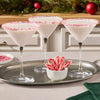 A hand reaches for a pinwheel cookie from a plate filled with many more, alongside glasses of milk.