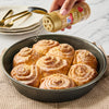 A hand sprinkles McCormick cinnamon sugar onto a pan of freshly baked cinnamon rolls.
