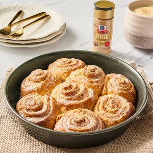 A pan of freshly baked cinnamon rolls with icing, alongside a McCormick Cinnamon Sugar blend.