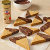A batch of triangle-shaped shortbread cookies, half dipped in chocolate and sprinkled with McCormick brand cinnamon sugar, are arranged on parchment paper next to a bowl of chocolate sauce and a McCormick cinnamon sugar container.