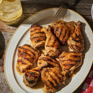 ['A plate of grilled chicken thighs with a side of lemon water.']