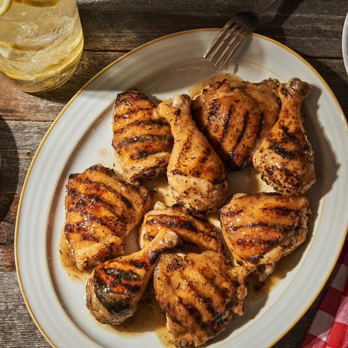 ['A plate of grilled chicken thighs with a side of lemon water.']