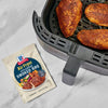 McCormick Air Fryer Sweet &amp; Smoky BBQ seasoning mix is shown next to an air fryer with seasoned chicken inside.