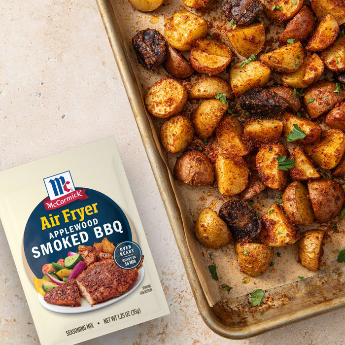 A package of McCormick Air Fryer Smoked BBQ seasoning is displayed next to a sheet pan of seasoned and cooked potatoes.