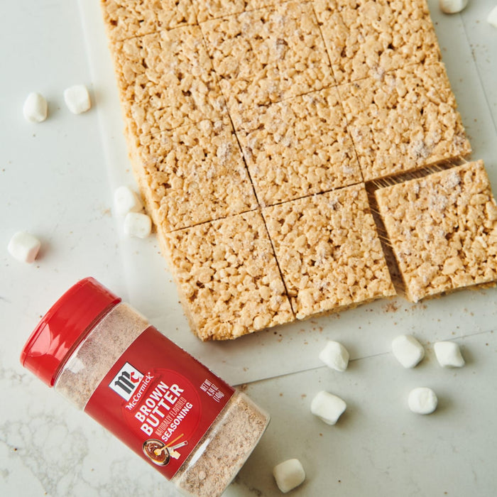 ['A container of McCormick Brown Butter seasoning next to a plate of rice crispy treats.']