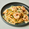 ['A plate of pasta with shrimp, parmesan cheese, and parsley.']