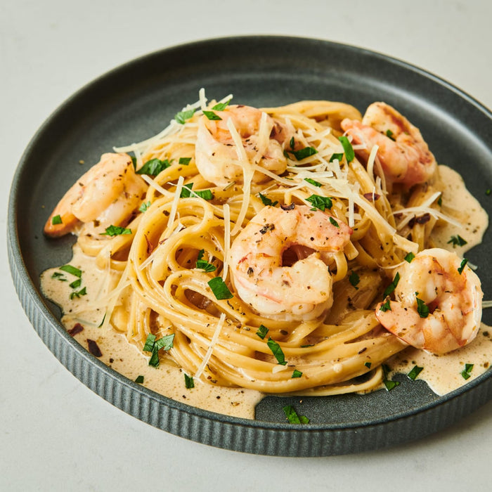 ['A plate of pasta with shrimp, parmesan cheese, and parsley.']
