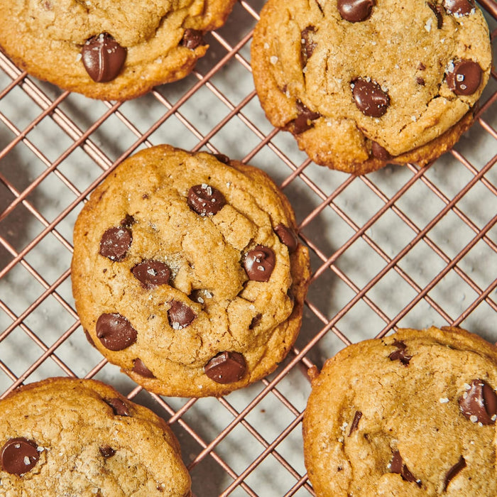 ['Four chocolate chip cookies on a wire rack.']