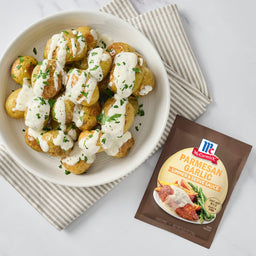 A plate of potatoes drizzled with McCormick Parmesan Garlic Sauce is displayed next to the sauce packet.