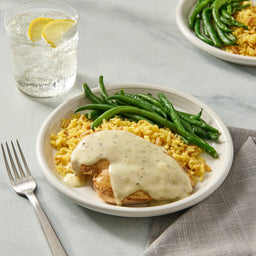 A plated meal of chicken breast topped with a creamy sauce made from Mccormick Lemon Herb Butter All Purpose Sauce Mix Envelope .87 Oz, served with yellow rice and green beans.