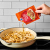 A hand pours McCormick Chicken Taco seasoning into a pan of cooked chicken.