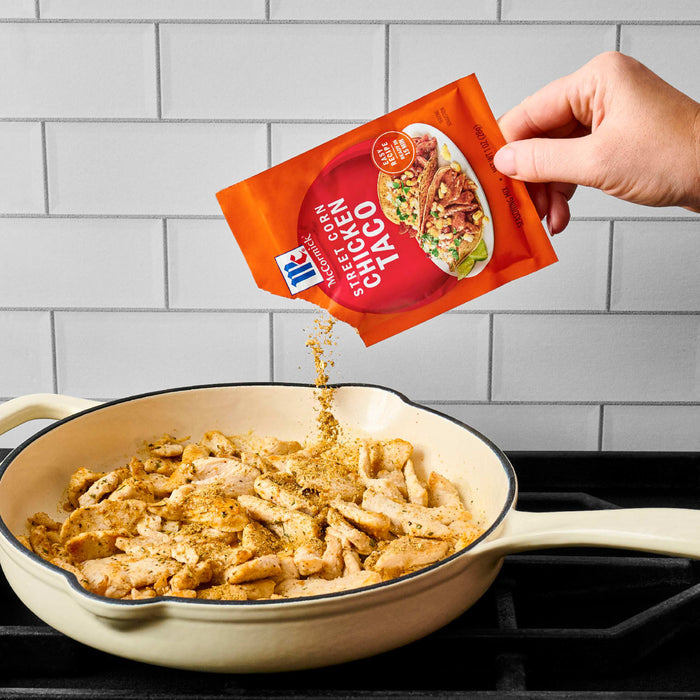 A hand pours McCormick Chicken Taco seasoning into a pan of cooked chicken.