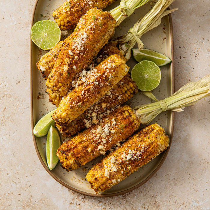 A platter of grilled corn on the cob, prepared Elote style with lime wedges.