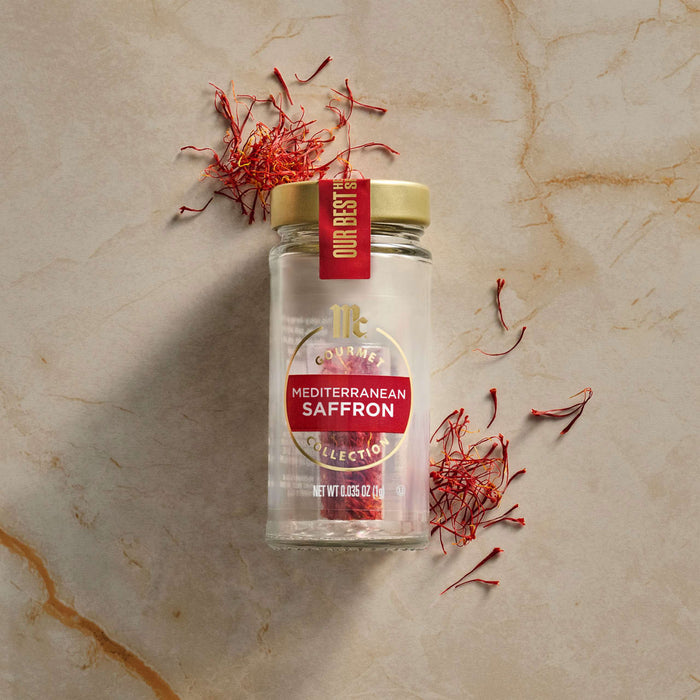 A glass jar of Mccormick Gourmet Saffron 0.035 Oz is displayed on a light marble surface, surrounded by scattered vibrant red saffron threads.