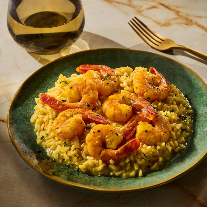 A plate of shrimp risotto is presented with a glass of white wine and a gold fork, suggesting a fine dining experience.