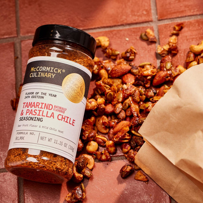 ['A jar of McCormick Culinary Tamarind &amp; Pasilla Chile Seasoning sits on a table with a bag of nuts.']