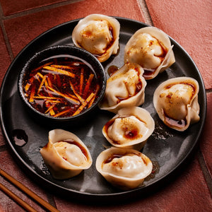 ['A plate of dumplings with a side of chili oil.']