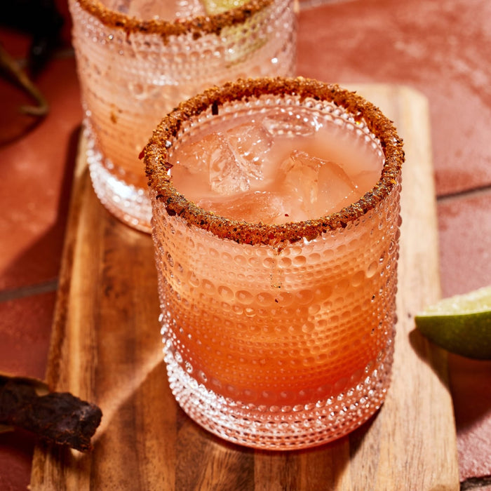 ['Two glasses of a pink drink with a brown rim on a wooden board.']