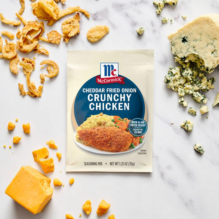 A packet of McCormick Cheddar Fried Onion Crunchy Chicken mix is displayed amidst scattered ingredients like fried onions, cheddar cheese, and blue cheese.