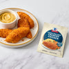A plate of crispy chicken tenders with a side of dipping sauce, alongside a packet of McCormick Shake 'n Bake Extra Crispy Seasoned Coating Mix.