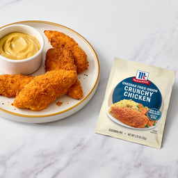 A plate of crispy chicken tenders with a side of dipping sauce, alongside a packet of McCormick Shake 'n Bake Extra Crispy Seasoned Coating Mix.