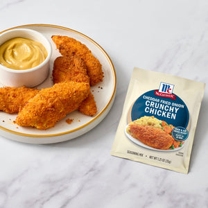 A plate of crispy chicken tenders with a side of dipping sauce, alongside a packet of McCormick Shake 'n Bake Extra Crispy Seasoned Coating Mix.