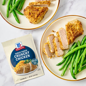 Two plates of sliced, breaded pork chops and green beans are displayed next to a packet of McCormick Flavor Maker Crunchy Chicken seasoning.