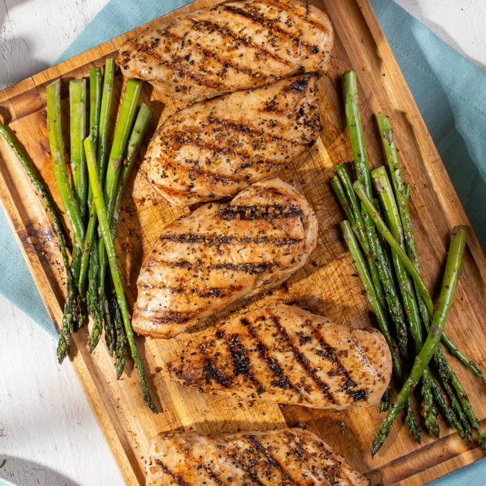 ['Grilled chicken breasts and asparagus spears on a wooden cutting board.']