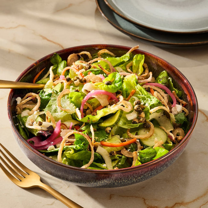 A vibrant salad with lettuce, red onions, and crispy noodles is presented in a decorative bowl.