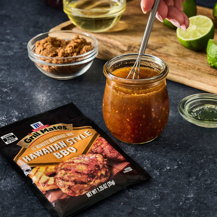['A packet of McCormick Grill Mates Hawaiian Style BBQ marinade mix is displayed next to a jar of marinade being whisked, with ingredients like brown sugar and lime nearby.']