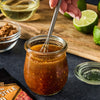 A packet of McCormick Grill Mates Hawaiian Style BBQ marinade mix is displayed next to a jar of marinade being whisked, with ingredients like brown sugar and lime nearby.