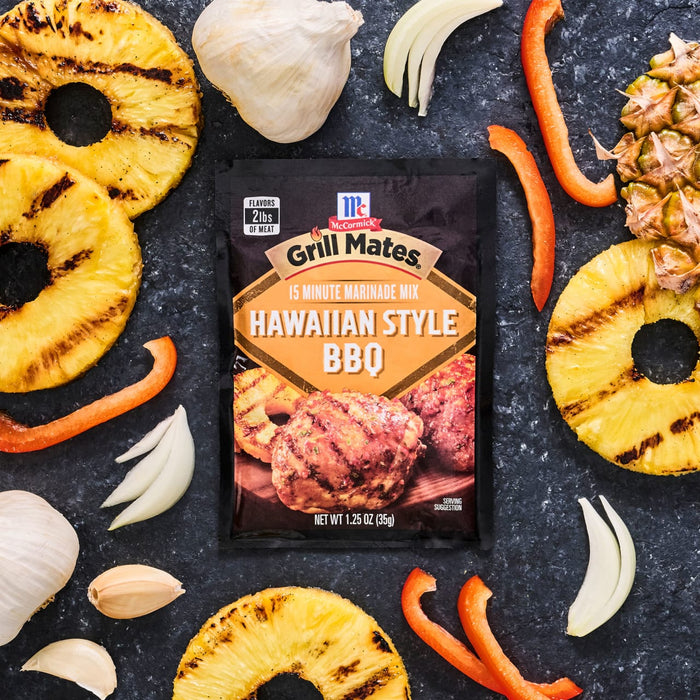 ['A package of McCormick Grill Mates Hawaiian Style BBQ marinade mix is surrounded by grilled pineapple rings, garlic cloves, onion slices, and red bell pepper strips.']