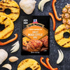 A package of McCormick Grill Mates Hawaiian Style BBQ marinade mix is surrounded by grilled pineapple rings, garlic cloves, onion slices, and red bell pepper strips.