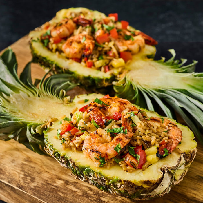 Two halves of a pineapple filled with shrimp and rice are displayed on a wooden board.
