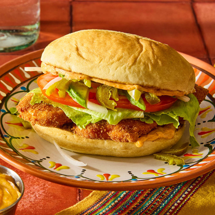 A close-up of a delicious-looking sandwich with fried chicken lettuce tomato avocado and jalapenos on a plate.