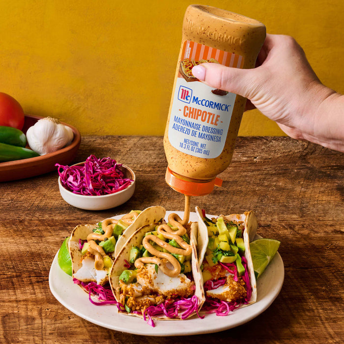 ['A hand is pouring McCormick Chipotle Mayonnaise Dressing onto fish tacos.']
