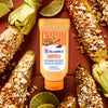 ['A bottle of McCormick Chipotle Mayonnaise Dressing with grilled corn on the cob topped with cheese and lime.']