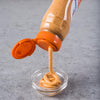['A bottle of a sauce is pouring into a small glass bowl.']