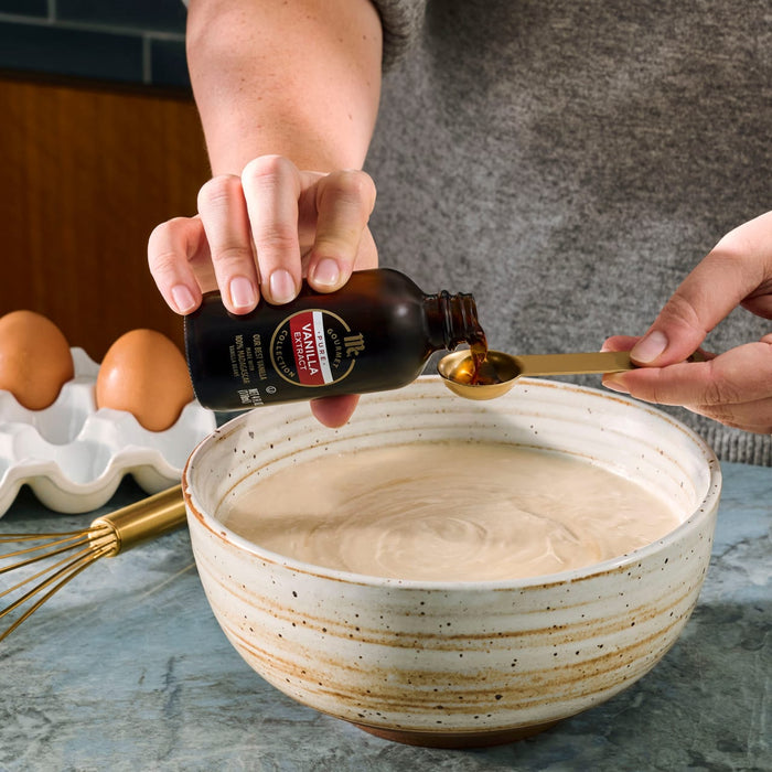 A person adds Nielsen-Massey vanilla extract to a bowl of batter while preparing a recipe.