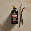 A bottle of Nielsen-Massey Vanilla Extract sits next to two vanilla beans.