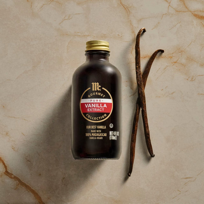 A bottle of Nielsen-Massey Vanilla Extract sits next to two vanilla beans.
