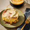 A frosted cinnamon roll sits on a plate next to a cup of coffee, suggesting a delicious breakfast or treat.